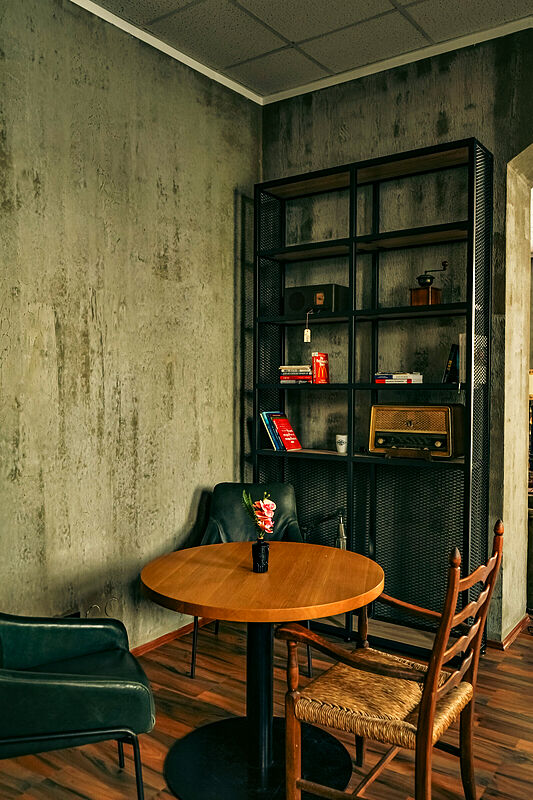 Ein runder Holztisch mit Kaffeehausstuhl und Sessel vor einem schwarzen Metallregal.