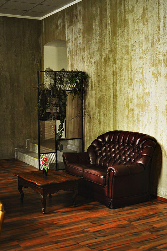 Ein dunkelrotes Ledersofa mit Couchtisch und Blume vor einer Wand in Betonoptik.
